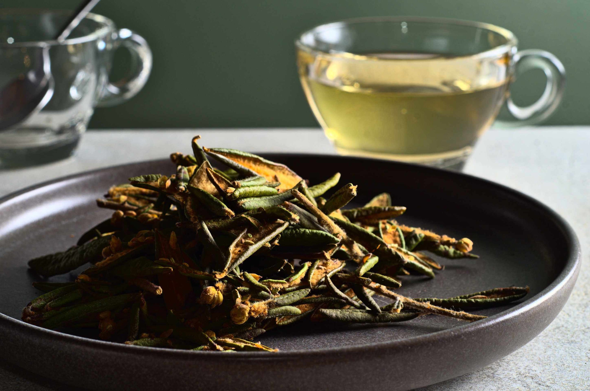 Herbes sauvages séchées sur assiette sombre avec tasse de tisane dorée en arrière-plan
