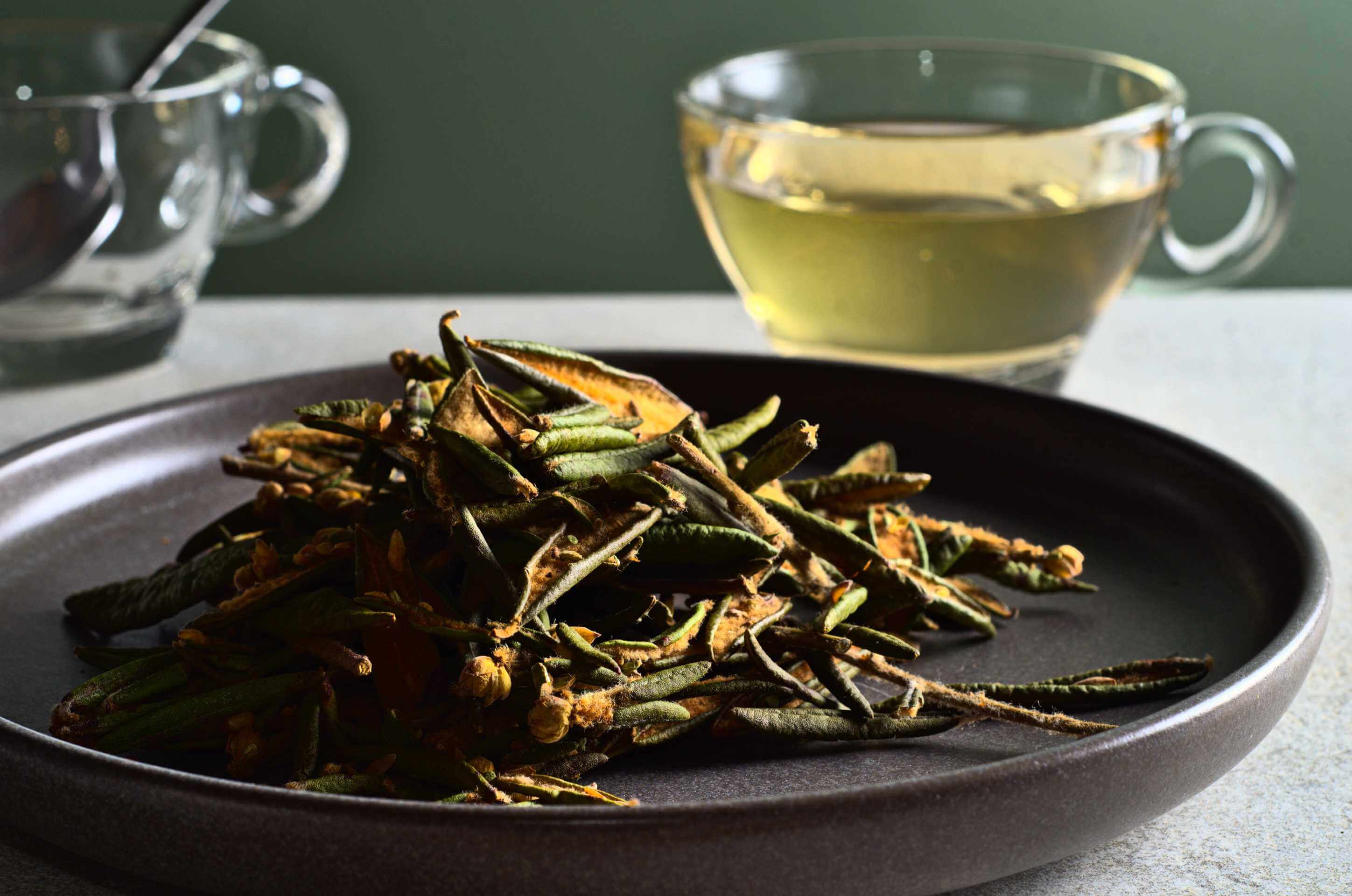 Herbes sauvages séchées sur assiette sombre avec tasse de tisane dorée en arrière-plan