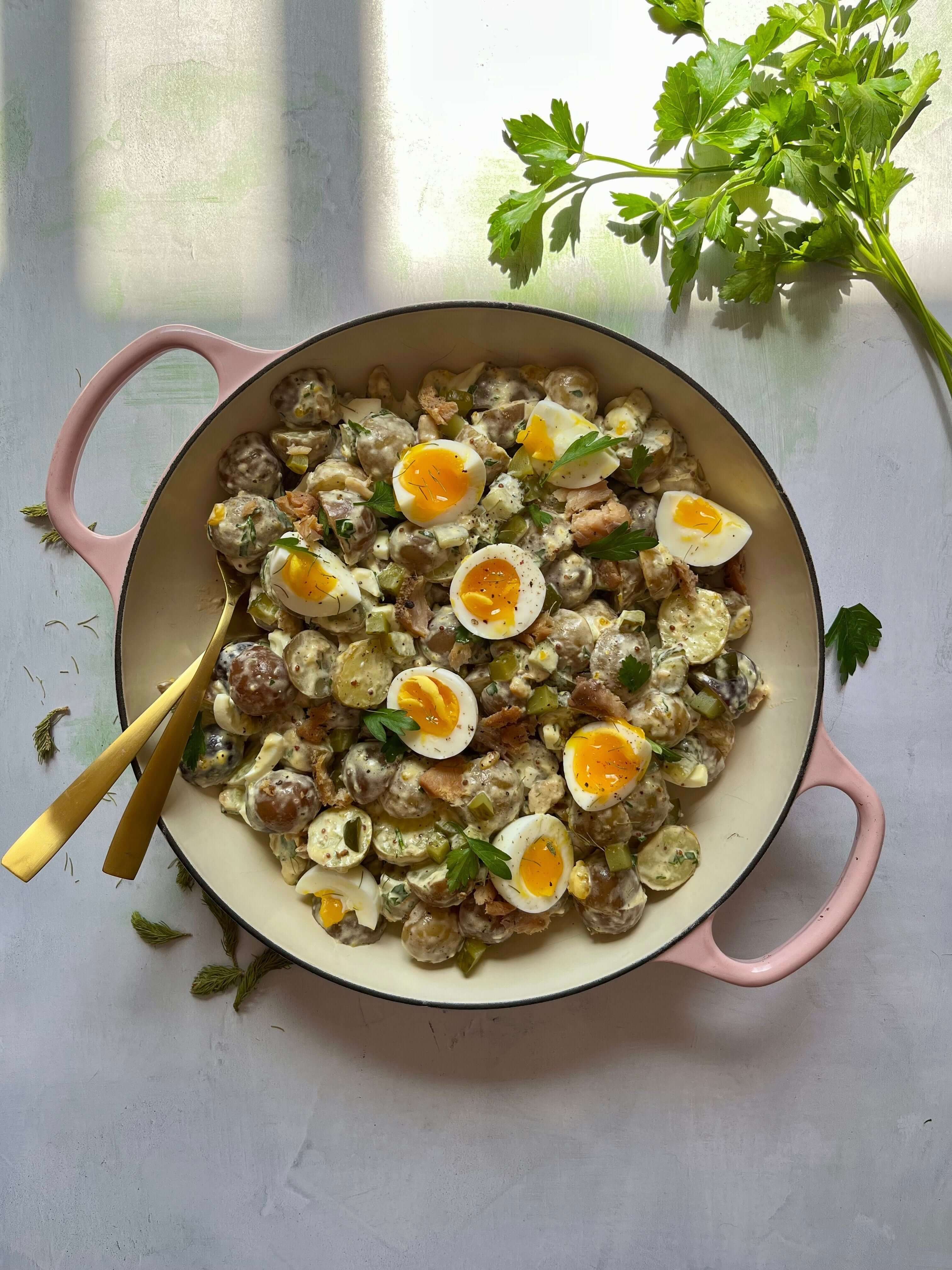 Salade de pommes de terre avec oeufs durs coupés, sauce crémeuse, herbes fraîches, dans cocotte rose