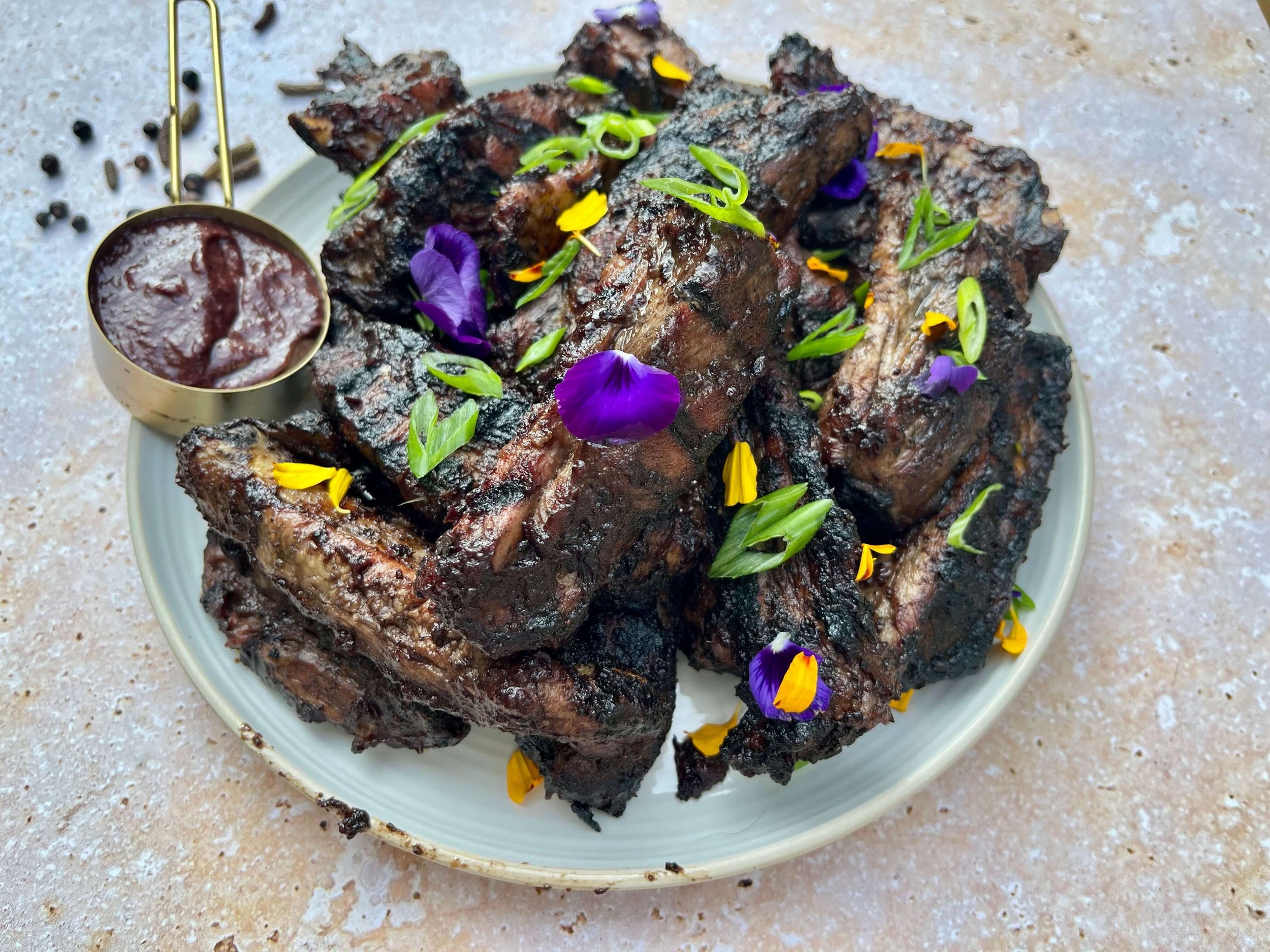 Côtes levées grillées nappées sauce BBQ foncée, garnies de fleurs comestibles et oignons verts