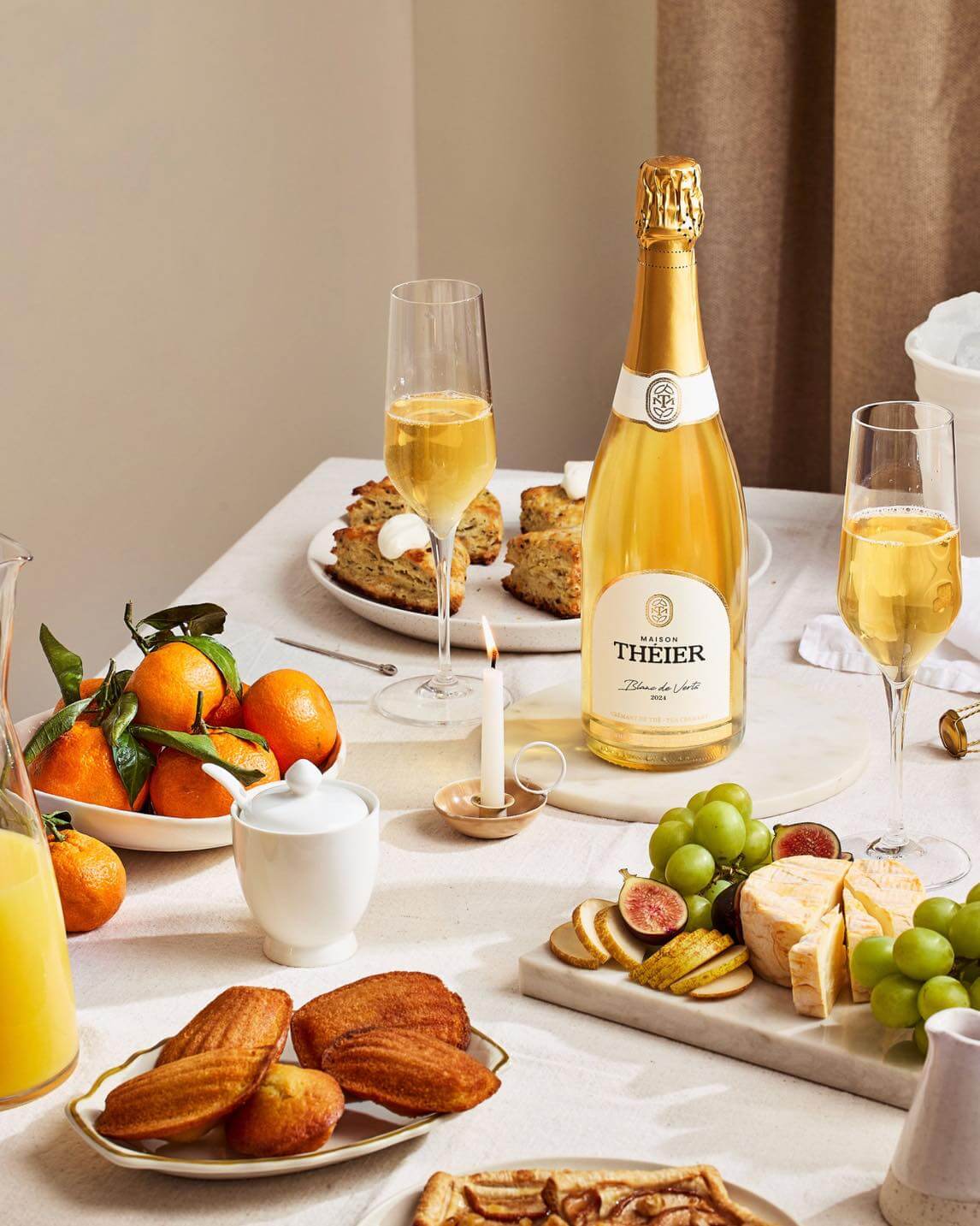 Table festive avec bouteille Maison Théier, coupes de bulles, madeleines, fromage, raisins et mandarines