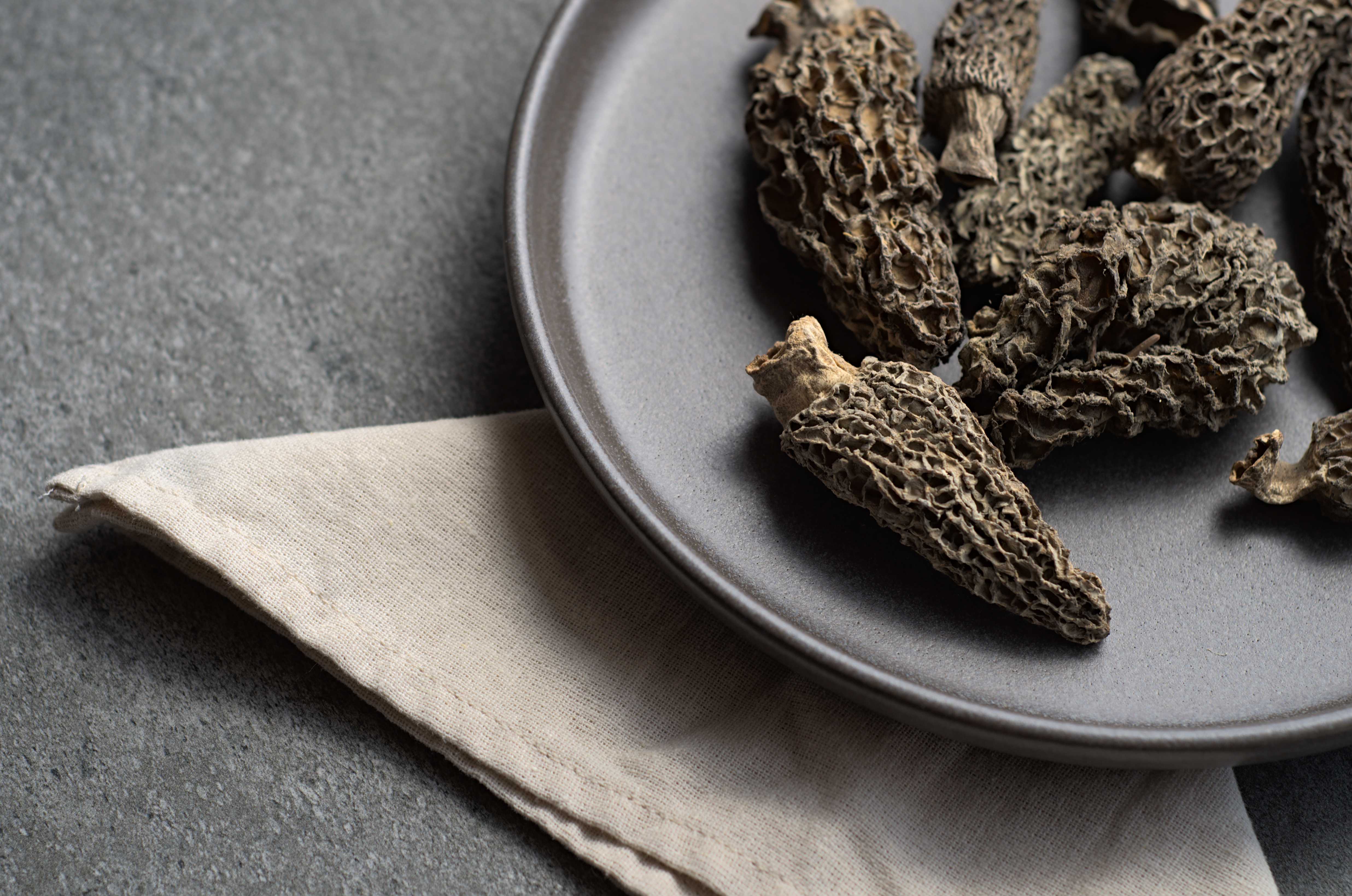 Morilles séchées entières sur assiette grise foncée avec serviette de lin, vue en gros plan