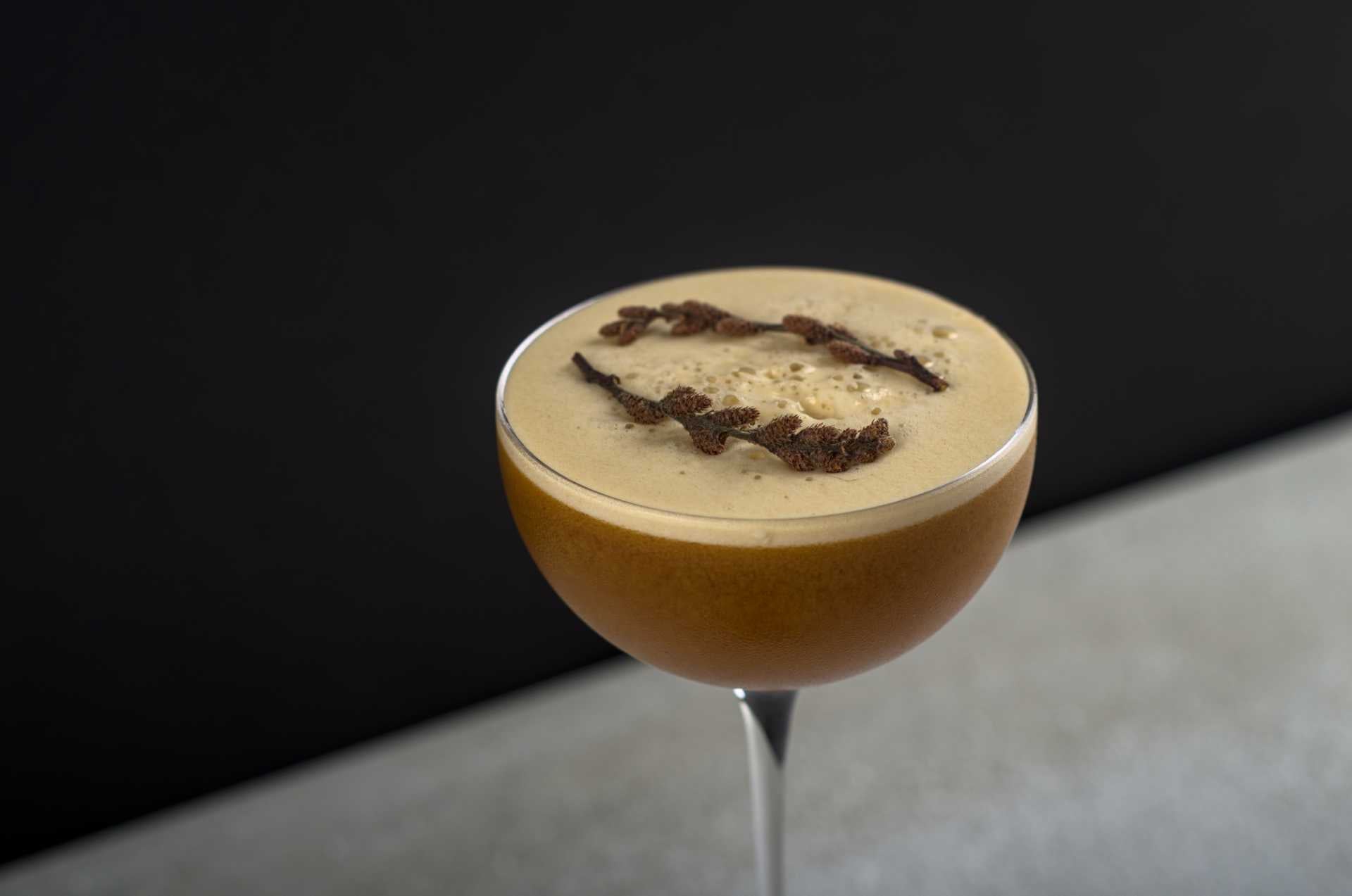 Cocktail mousseux garni de chatons d'aulne, dans une coupe sur fond noir