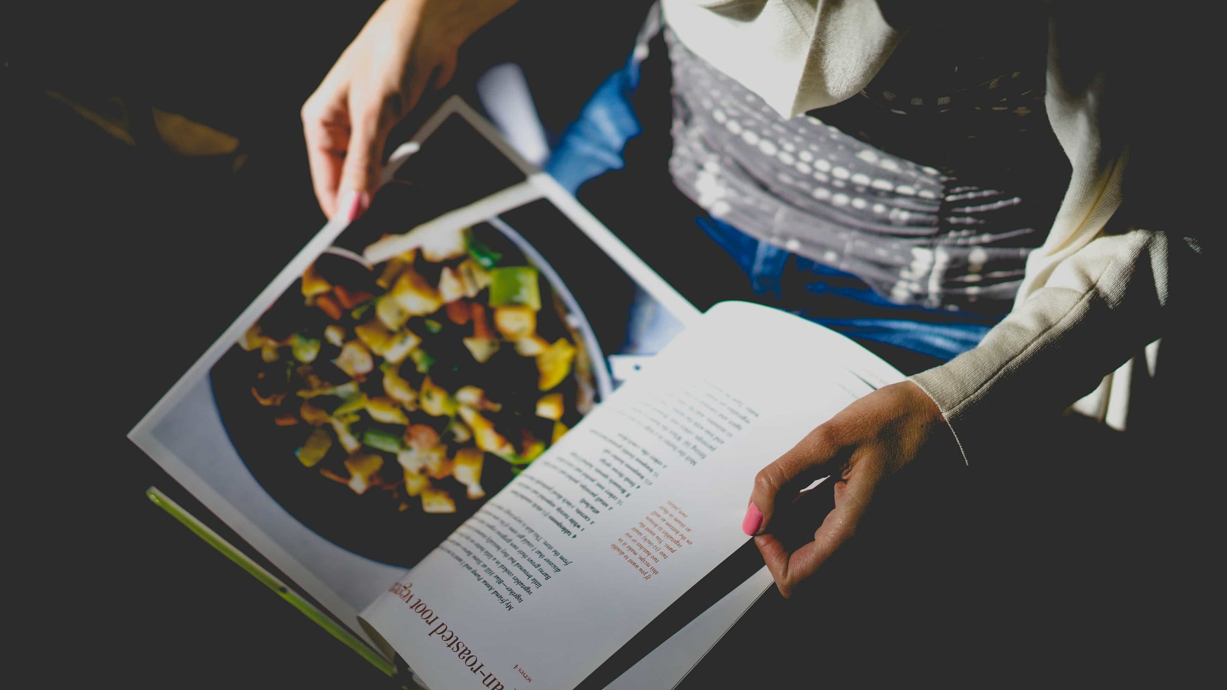 Personne feuilletant un livre de cuisine ouvert sur une recette de légumes rôtis