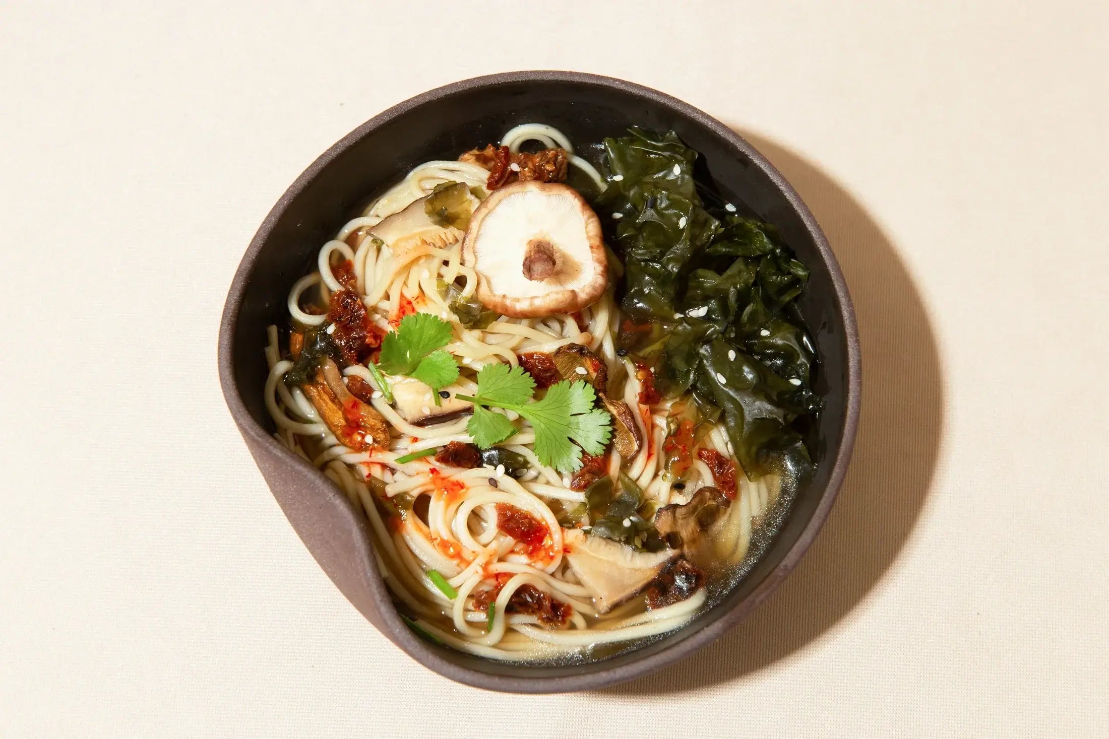 Bol de ramen aux champignons, algues et coriandre sur nappe crème