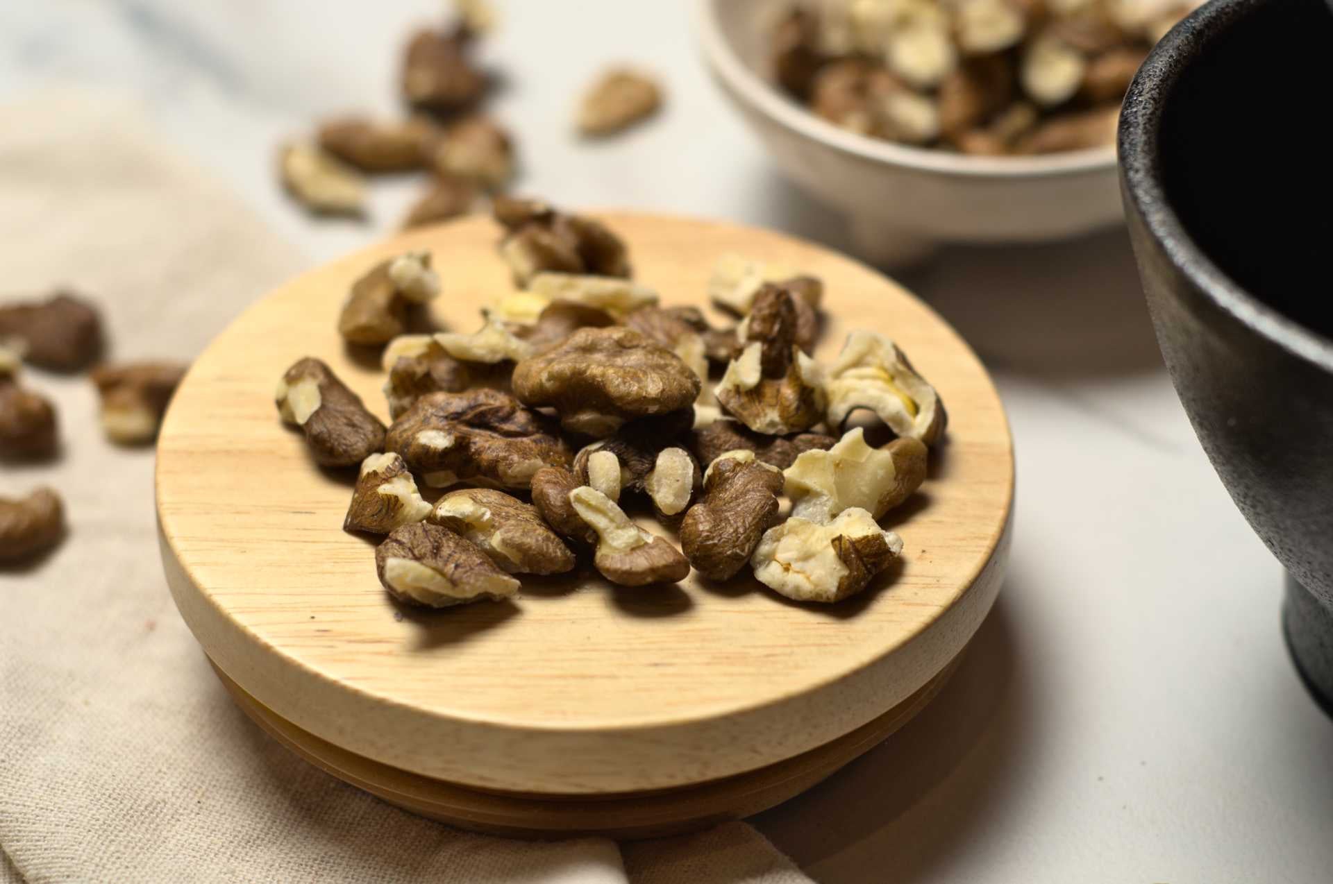 Noix de Grenoble décortiquées sur assiette de bois, entourées de noix entières