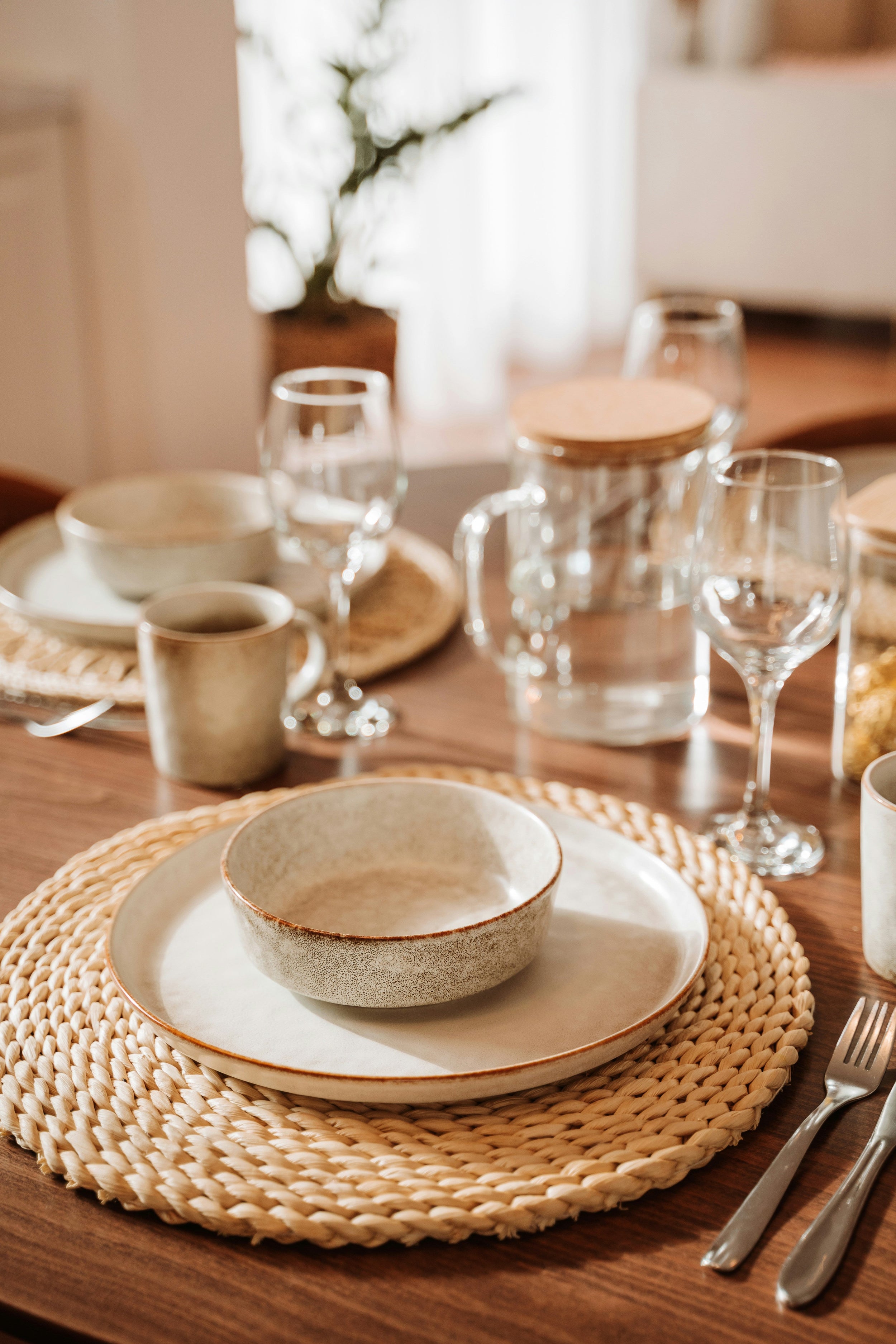 Table dressée avec vaisselle en grès, verres à vin et carafe, ambiance chaleureuse