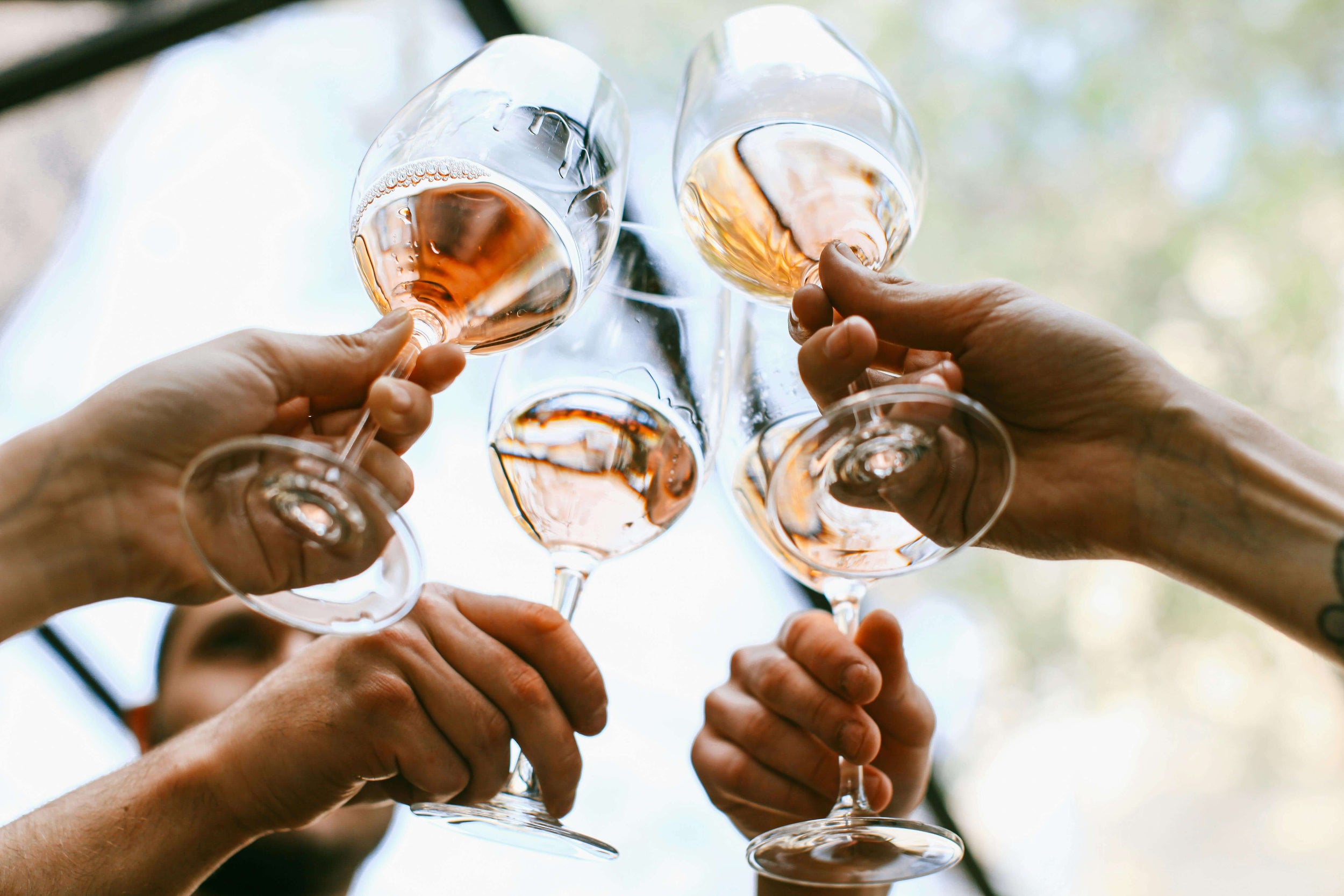 Quatre personnes trinquant avec des verres de vin rosé, vue du dessous en plein air
