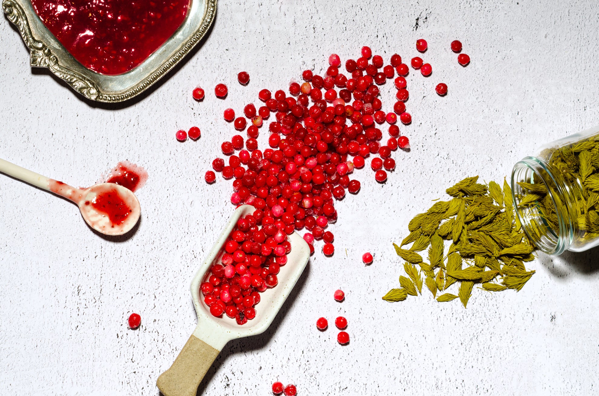 airelles congelées dans une petite pelle décorative en céramique, entourées de confiture et de pousses d'épinette sur fond blanc texturé