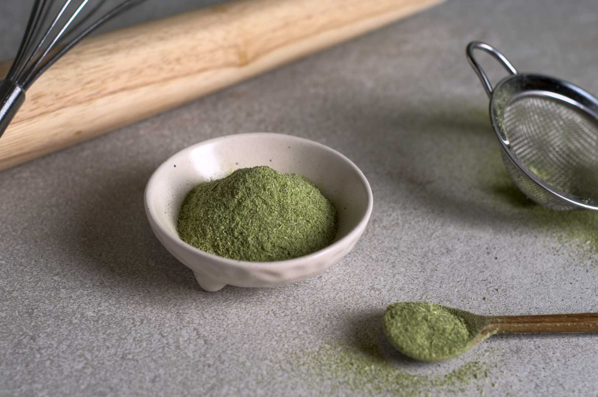 Fleur de mélilot avec tige en poudre (vanille boréale). La poudre de mélilot est placée dans un petit bol blanc sur un comptoir crème, avec un fouet, un rouleau à pâte, un tamis et une petite cuiller de bois. Le mur derrière est vert.