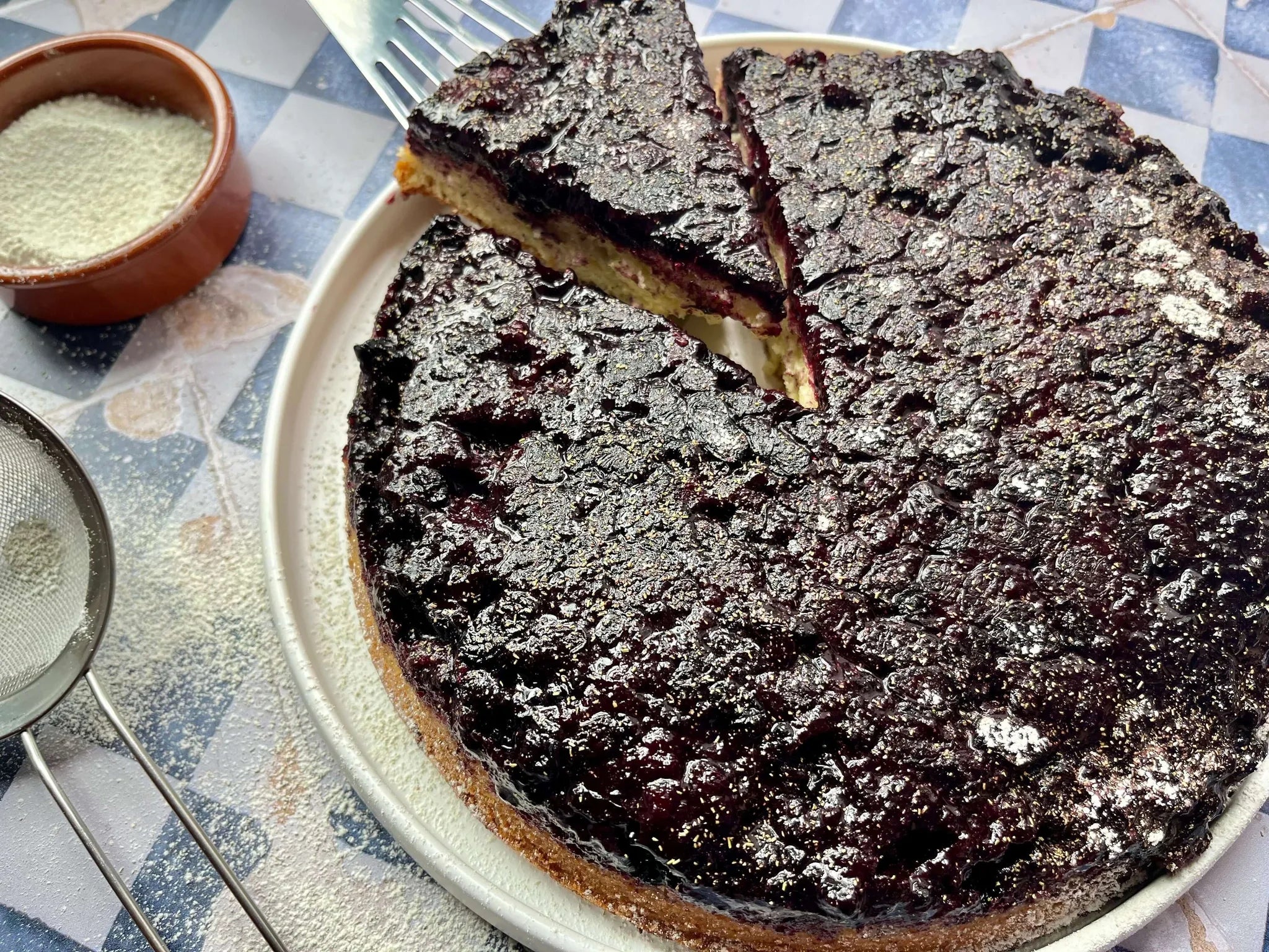Gâteau renversé aux camerises foncées et caramélisées, une portion retirée, sucre glace à côté