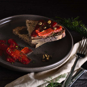 Tranches de gravlax de saumon déposées dans une assiette grise sur des tranches de pain. Le fond de l'image est noir.