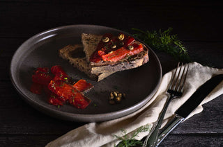 Tranches de gravlax de saumon déposées dans une assiette grise sur des tranches de pain. Le fond de l'image est noir.