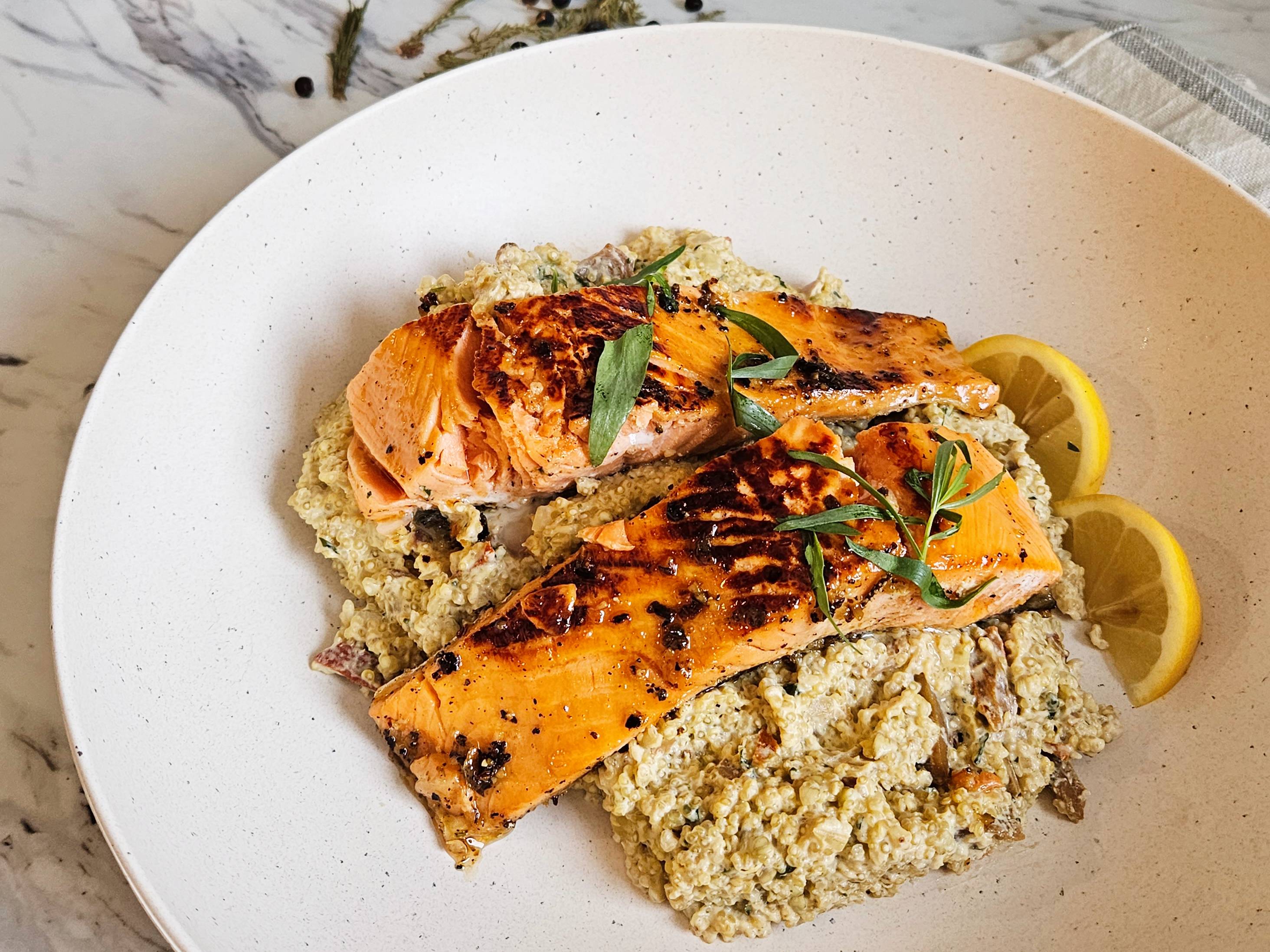 Filet de saumon aux baies de genévrier et au sapin baumier déposé sur une portion de quinoa crémeux aux champignons homards dans une assiette blanche