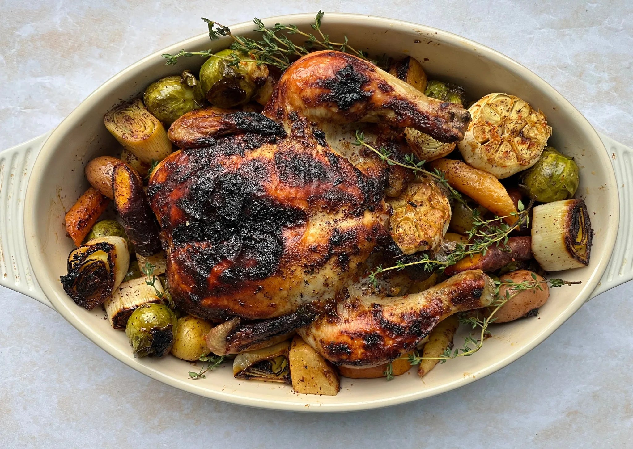 Poulet entier rôti doré dans plat ovale, entouré de choux de Bruxelles, pommes de terre et thym