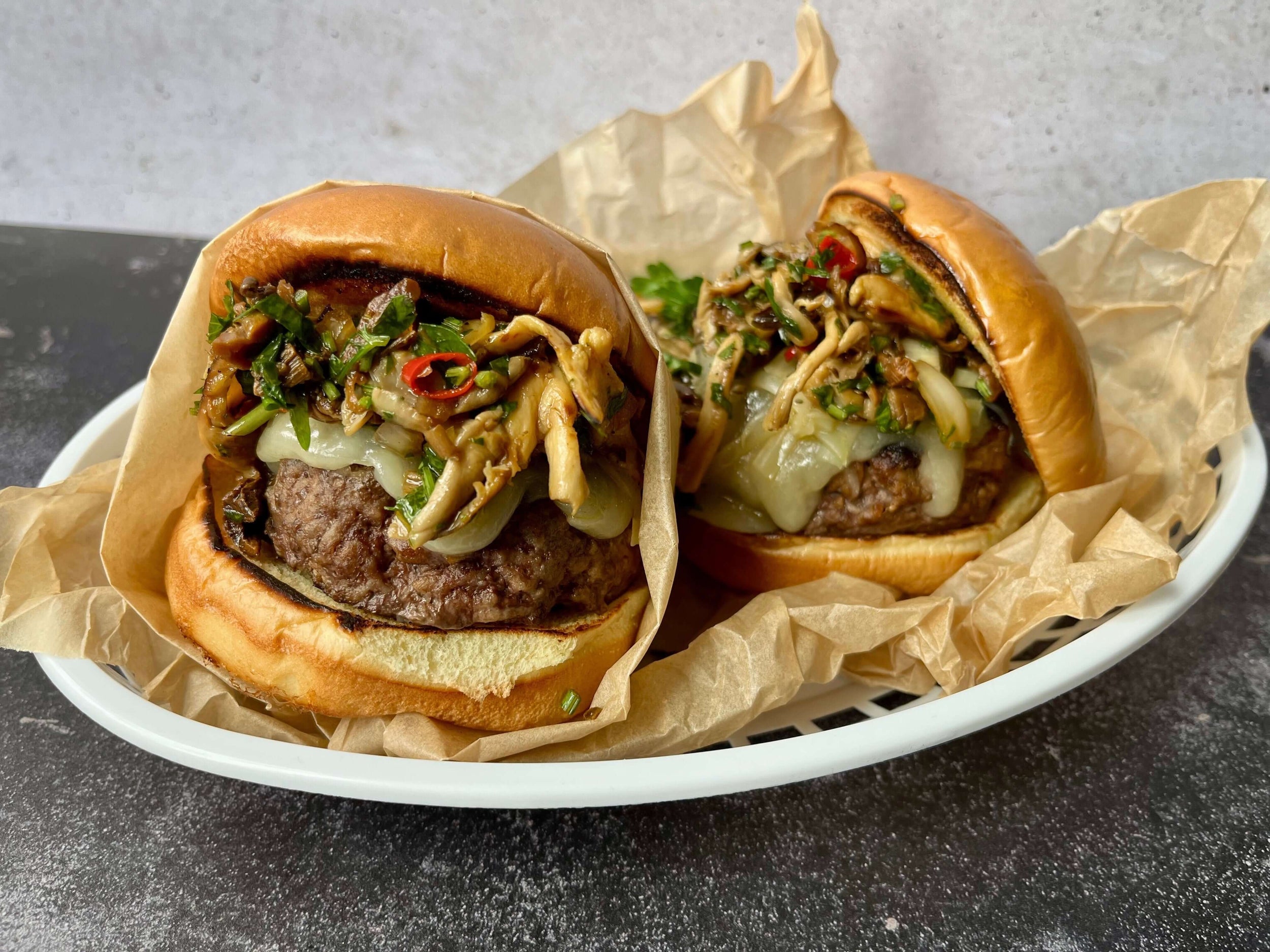 Deux burgers de boeuf avec fromage fondu, champignons et herbes dans paniers doublés de papier kraft