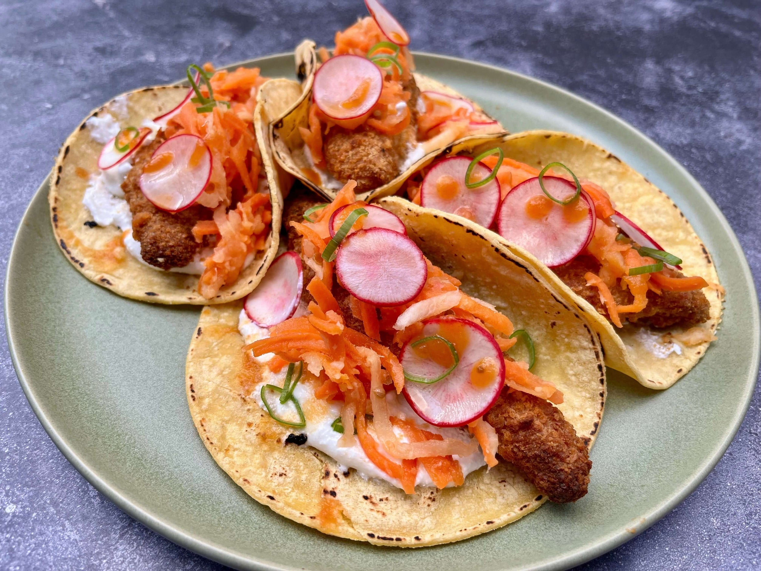 Trois tacos sur tortillas de maïs garnis de poisson croustillant, carottes râpées et radis marinés