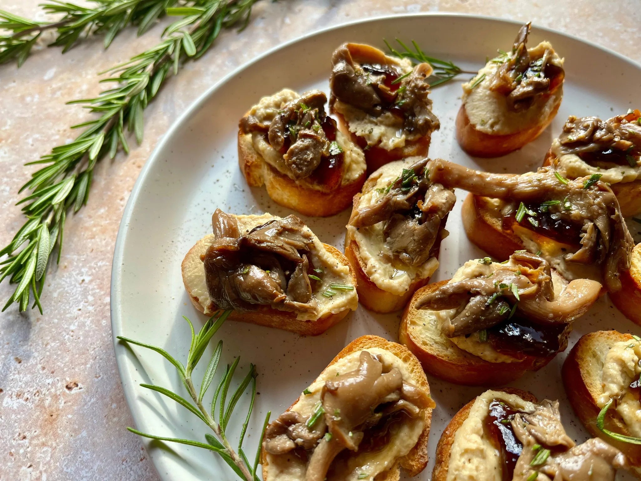 Assiette de crostinis dorés garnis de champignons marinés et houmous, brins de romarin frais