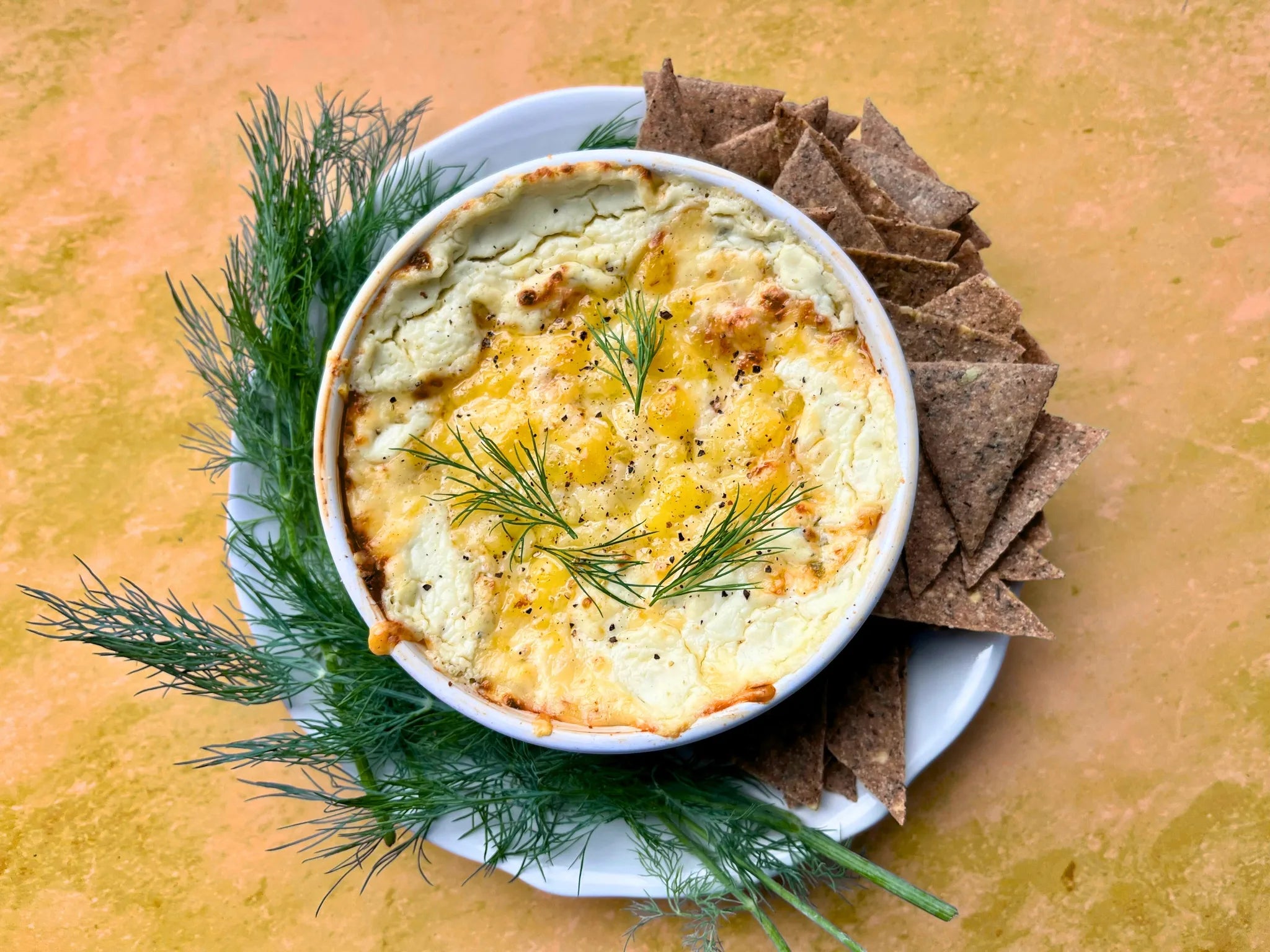 Trempette chaude gratinée dans ramequin blanc, garnie d'aneth frais, servie avec craquelins de seigle