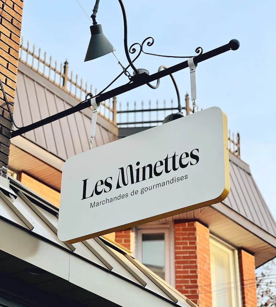 Enseigne suspendue de la boutique Les Minettes, marchandes de gourmandises, devant un bâtiment en brique