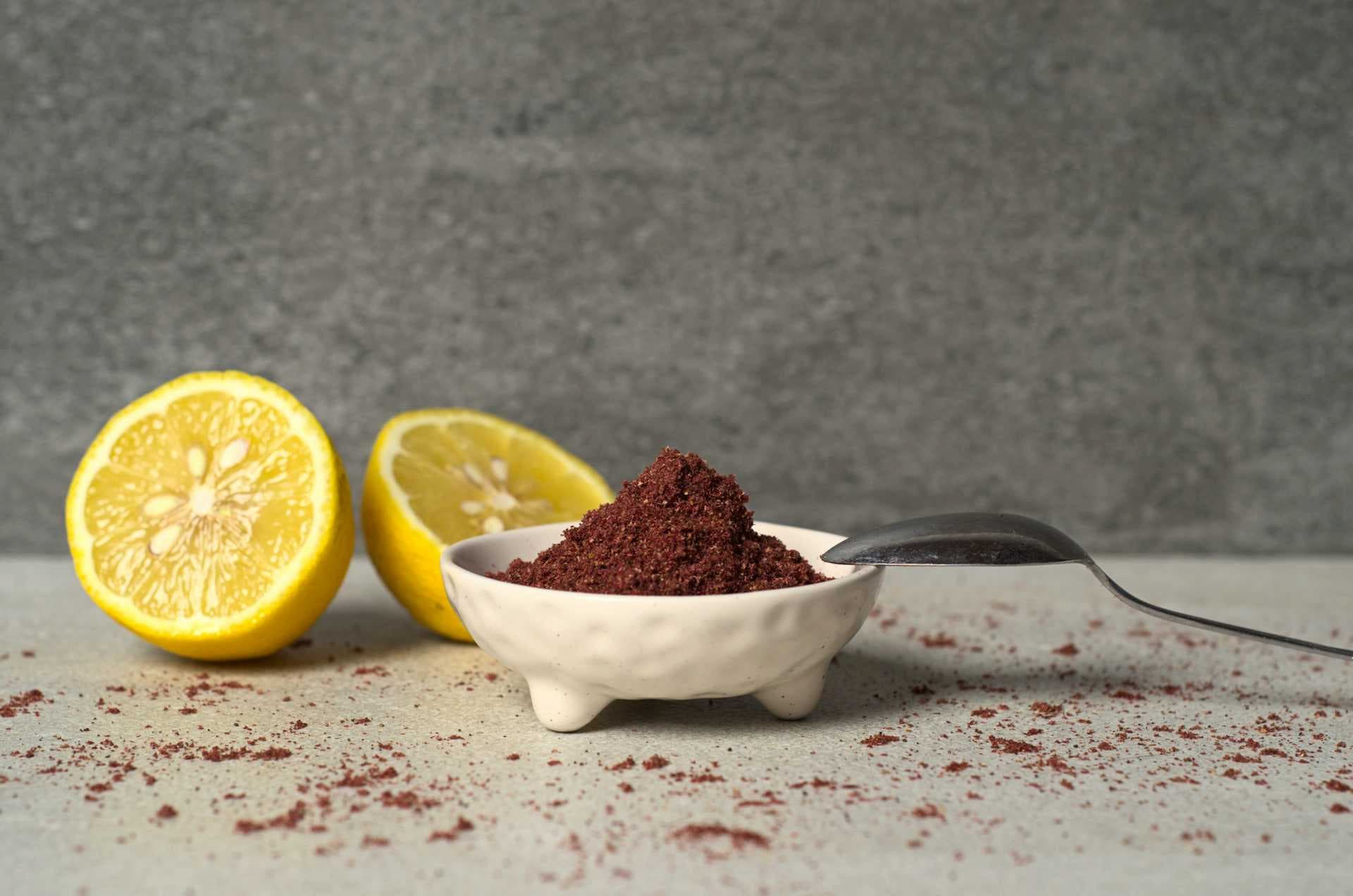 Sumac vinaigrier en poudre dans un bol blanc sur un comptoir, accompagné de citron tranché