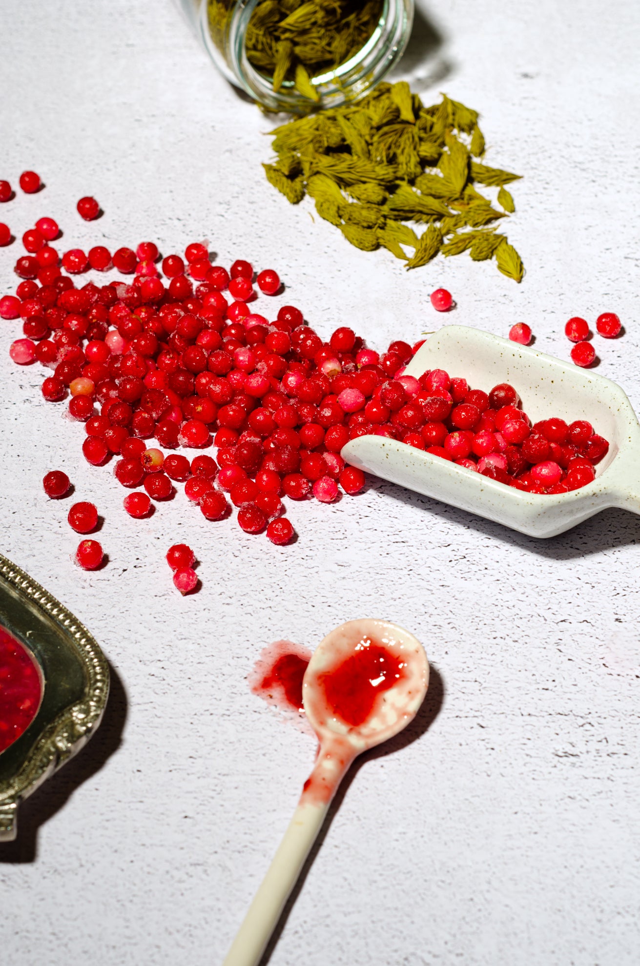 airelles congelées dans une petite pelle décorative en céramique, entourées de confiture et de pousses d'épinette sur fond blanc texturé