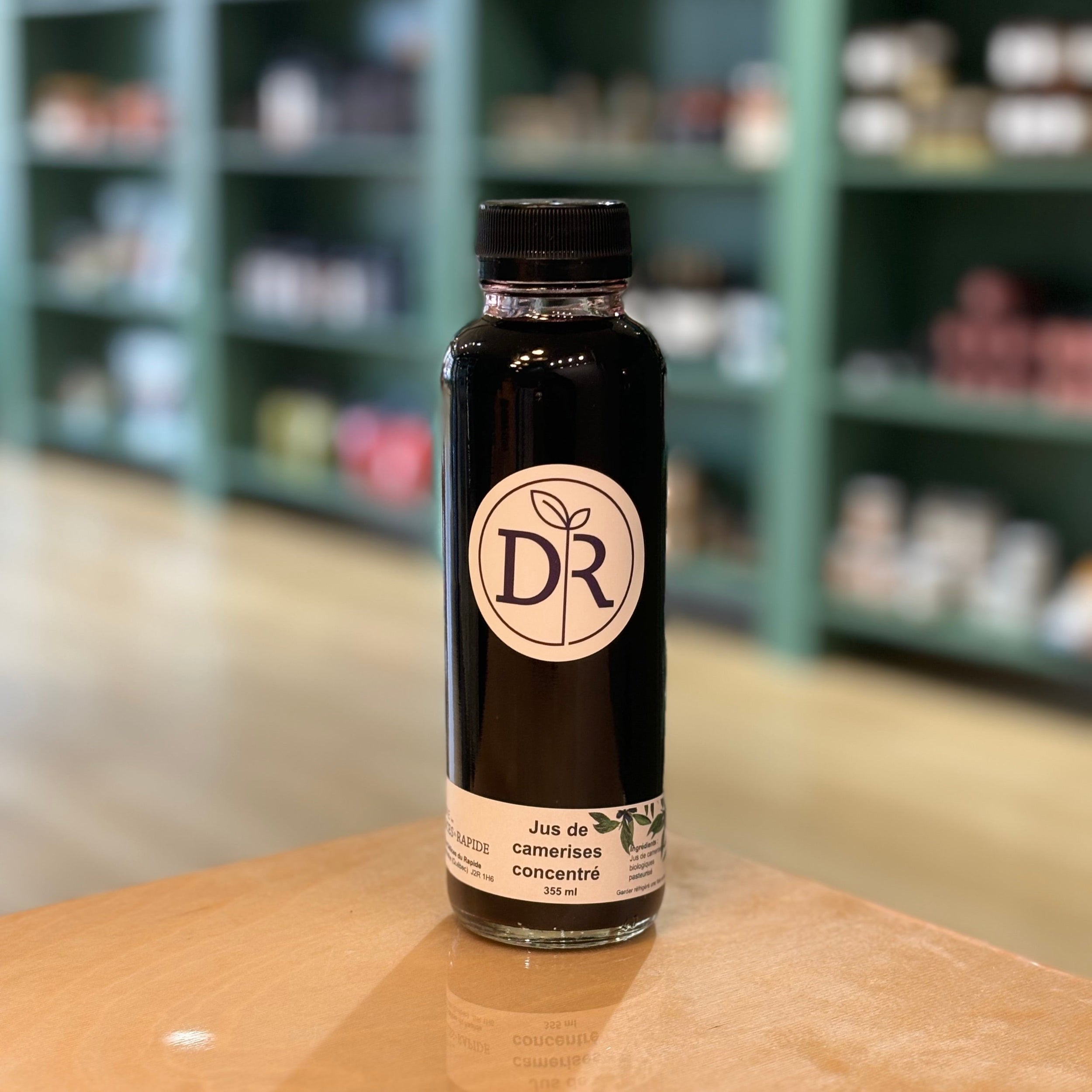 Bouteille en verre 355ml de jus de camerises biologiques concentré, étiquette blanche avec logo DR, photographiée en magasin