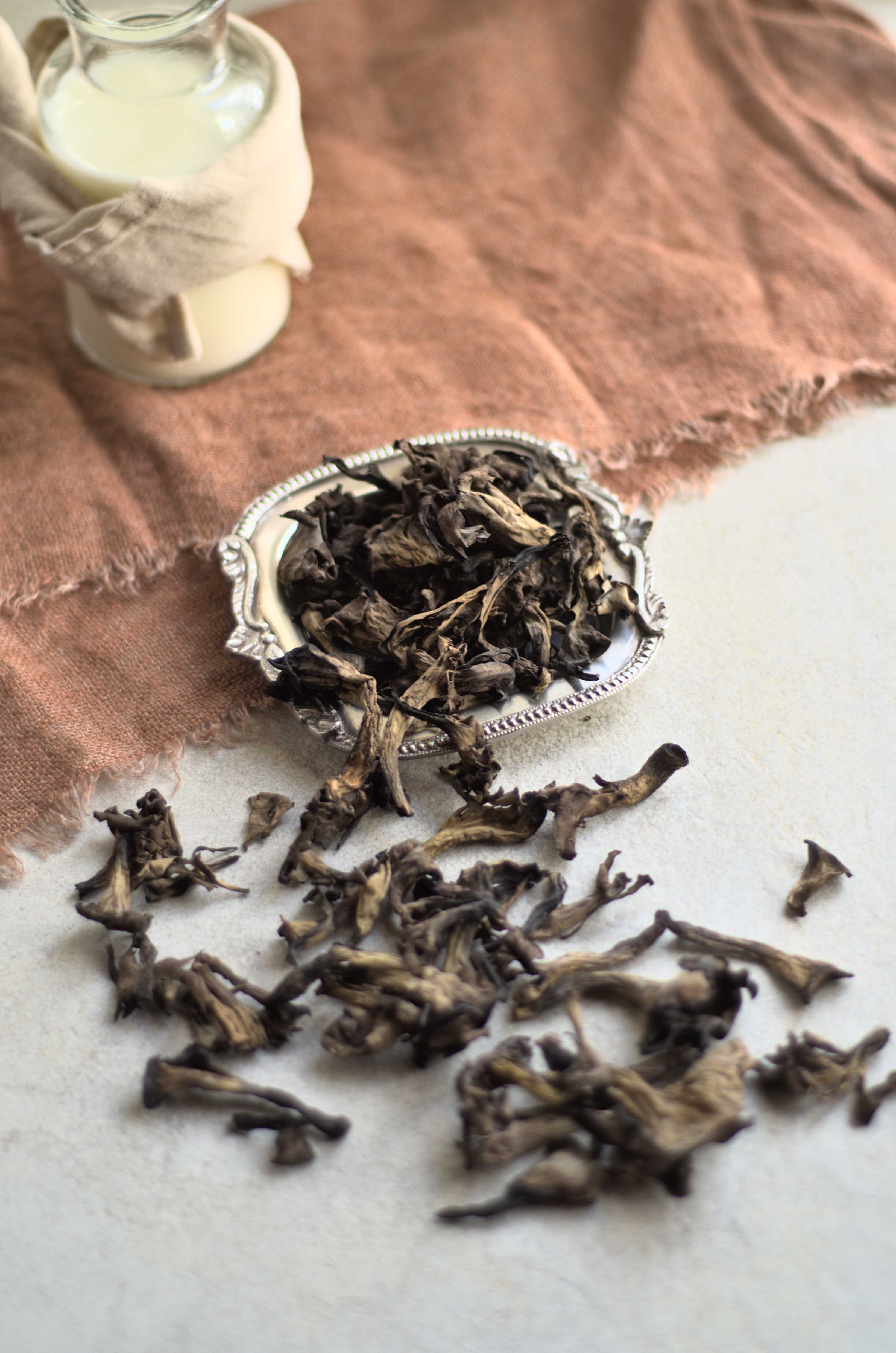 Champignons cornes d'abondance, ou trompettes de la mort, photographiées sur fond crème avec une serviette de table en lin vieux rose et un pot en verre rempli de lait.