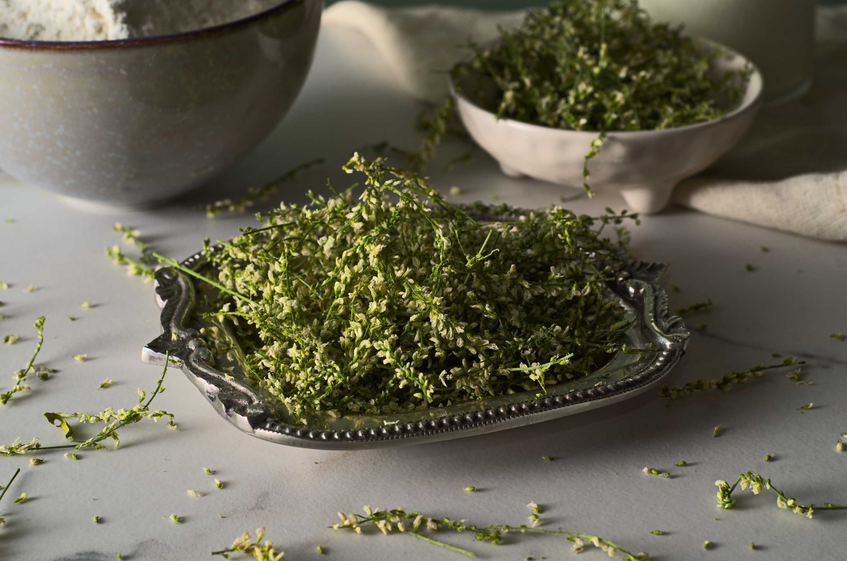 Plan rapproché de tiges et fleurs de mélilot blanc du Québec. L'aromate, aussi appelé vanille boréale ou vanille nordique, est déposé dans un plat métallique sur une surface en marbre.