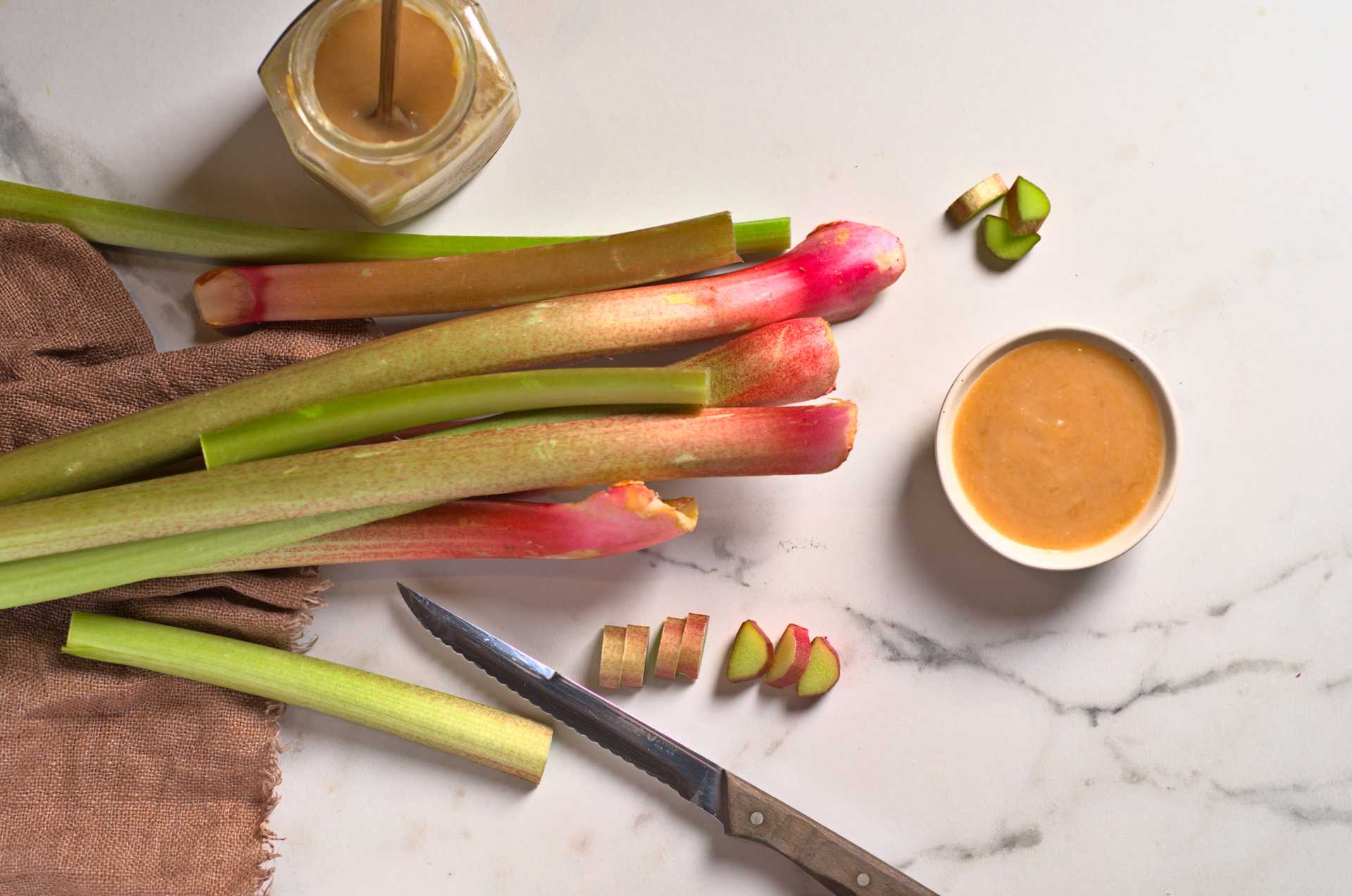 Rhubarbe fraîche en tiges avec compote de rhubarbe sur un comptoir en marbre blanc