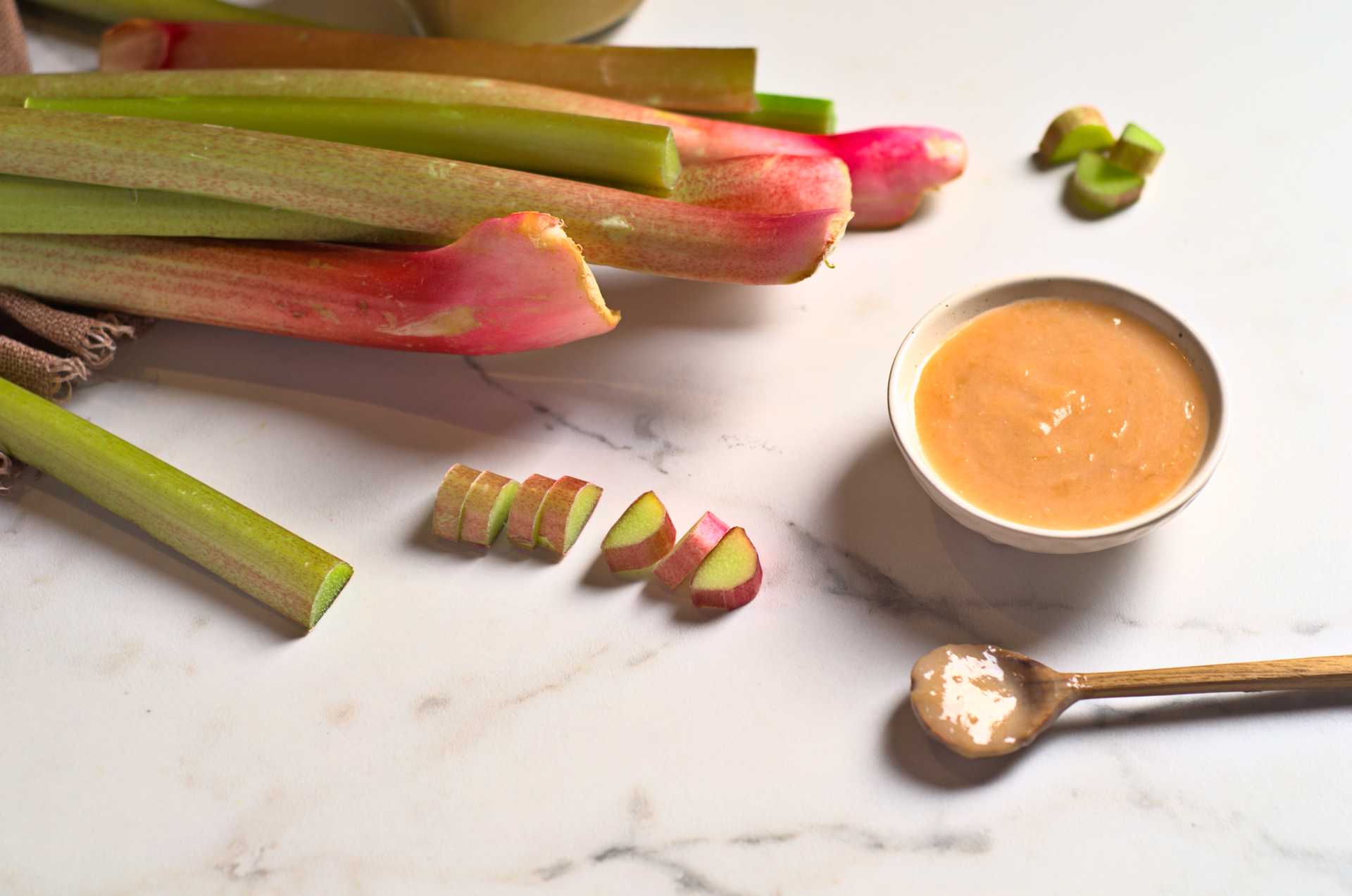 Rhubarbe fraîche en tiges avec compote de rhubarbe sur un comptoir en marbre blanc